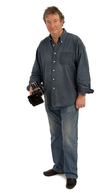 Portrait of Robert K Wilson standing against a white background, holding a camera