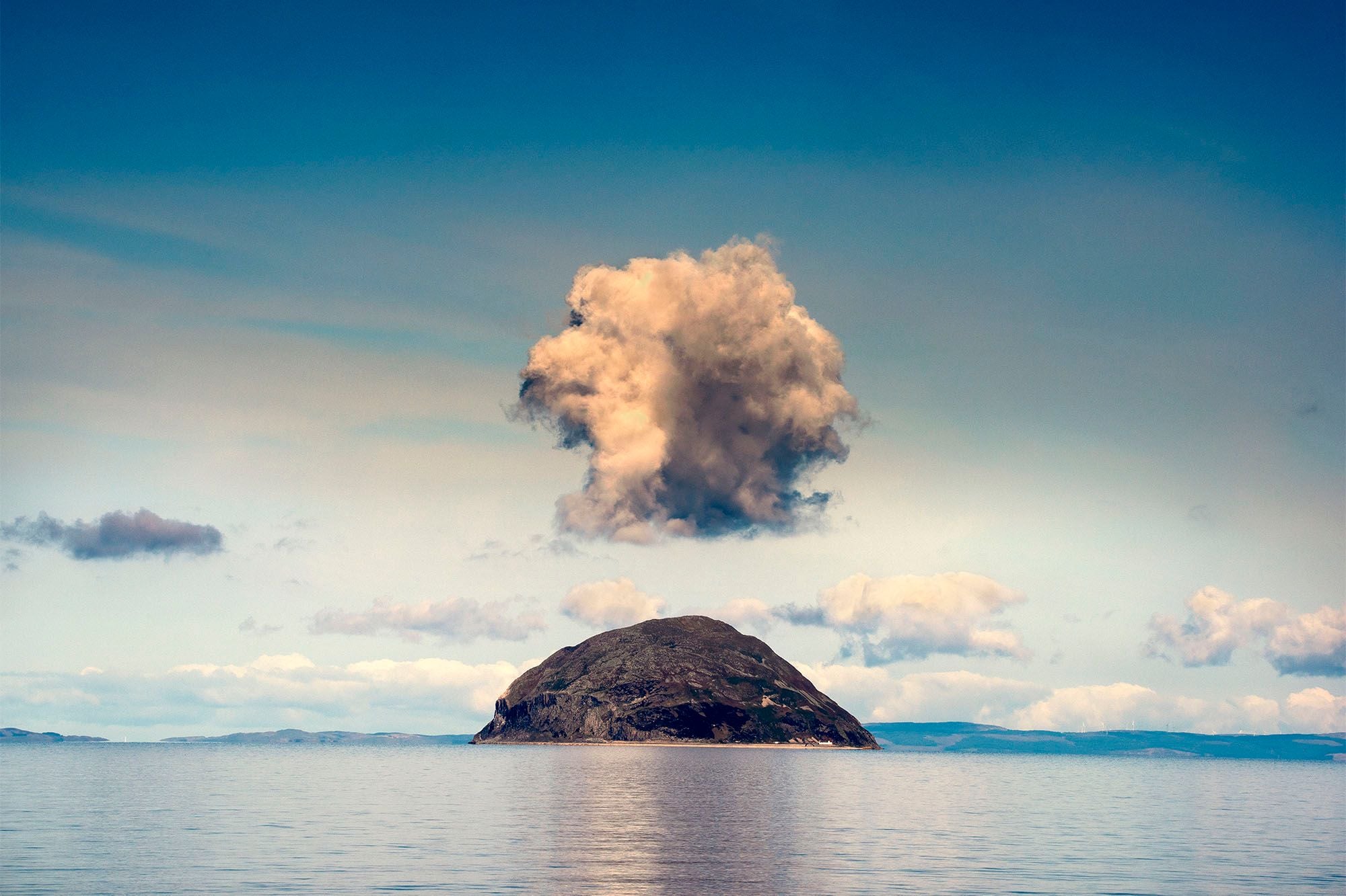 Ailsa Craig on a calm sea with a single towering cloud standing directly above it