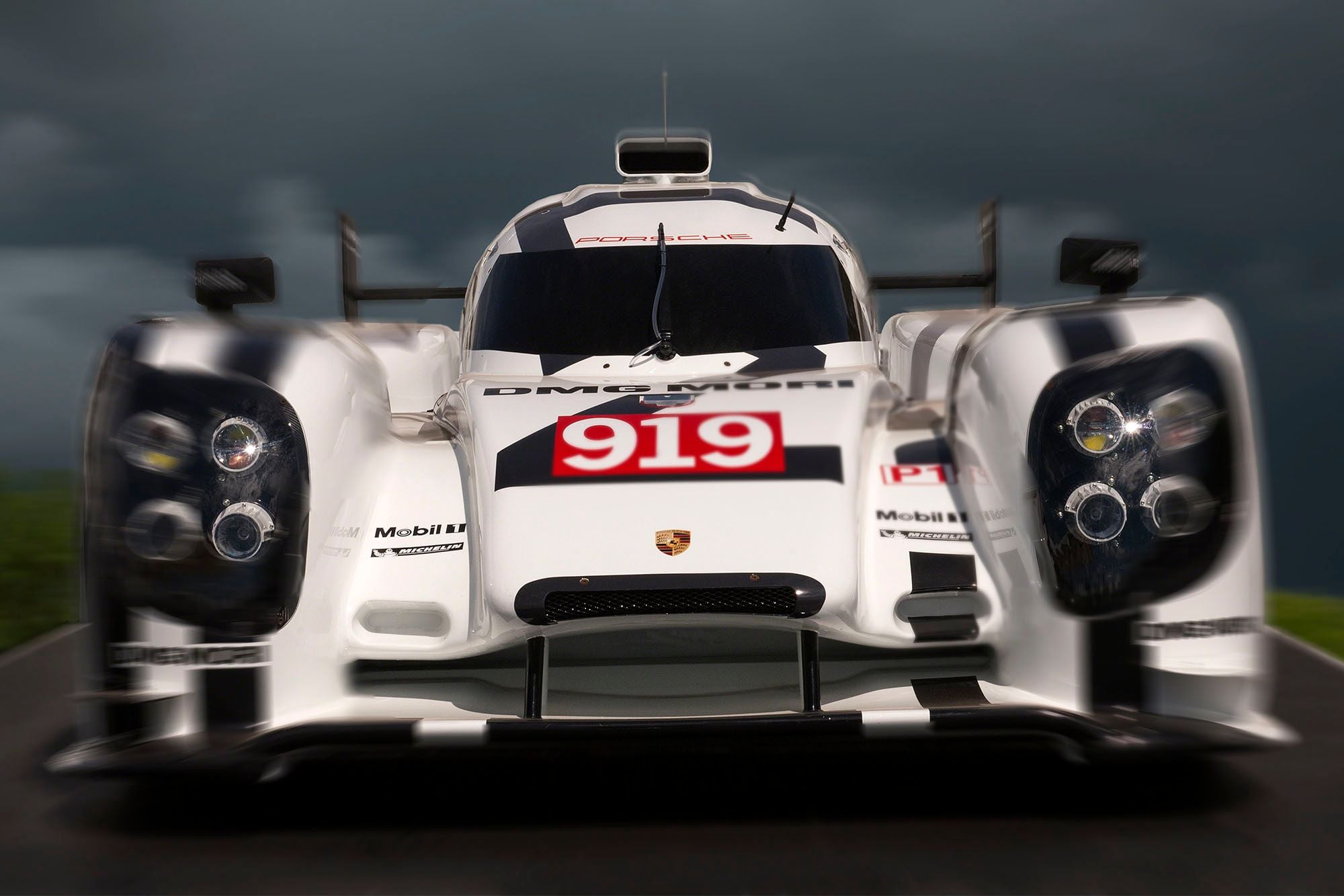 Front view of the white Porsche 919 Le Mans racing car, number 919, against a dark stormy sky