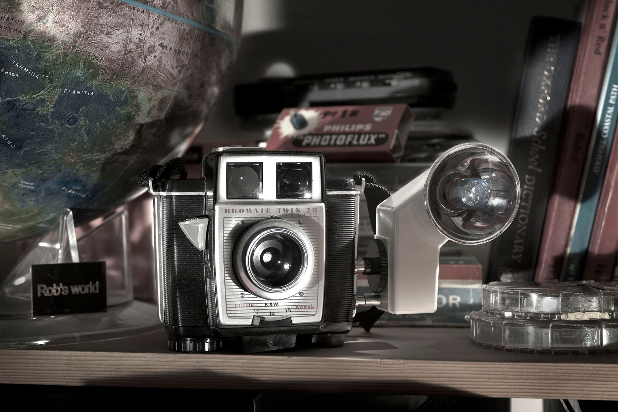 A Kodak Brownie Twin 20 camera and flashgun on a shelf beside an old globe and books